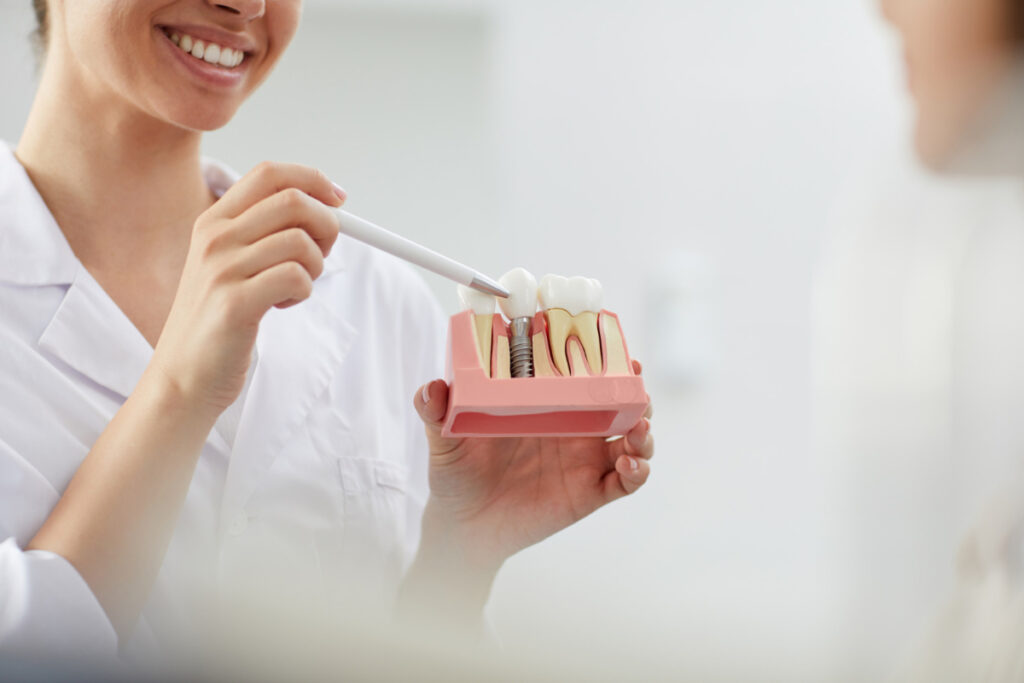 Uśmiechnięta dentystka prezentuje model korony zębowej na implancie