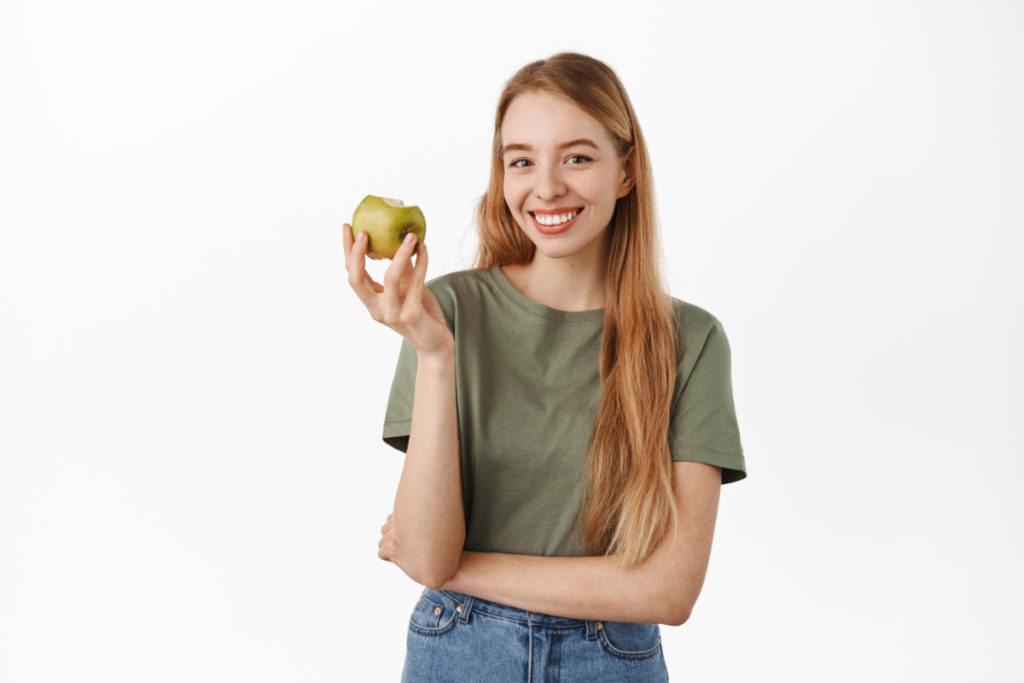 Uśmiechnięta dziewczyna z jabłkiem w dłoni. Usunięcie zęba - sposoby na jego uniknięcie