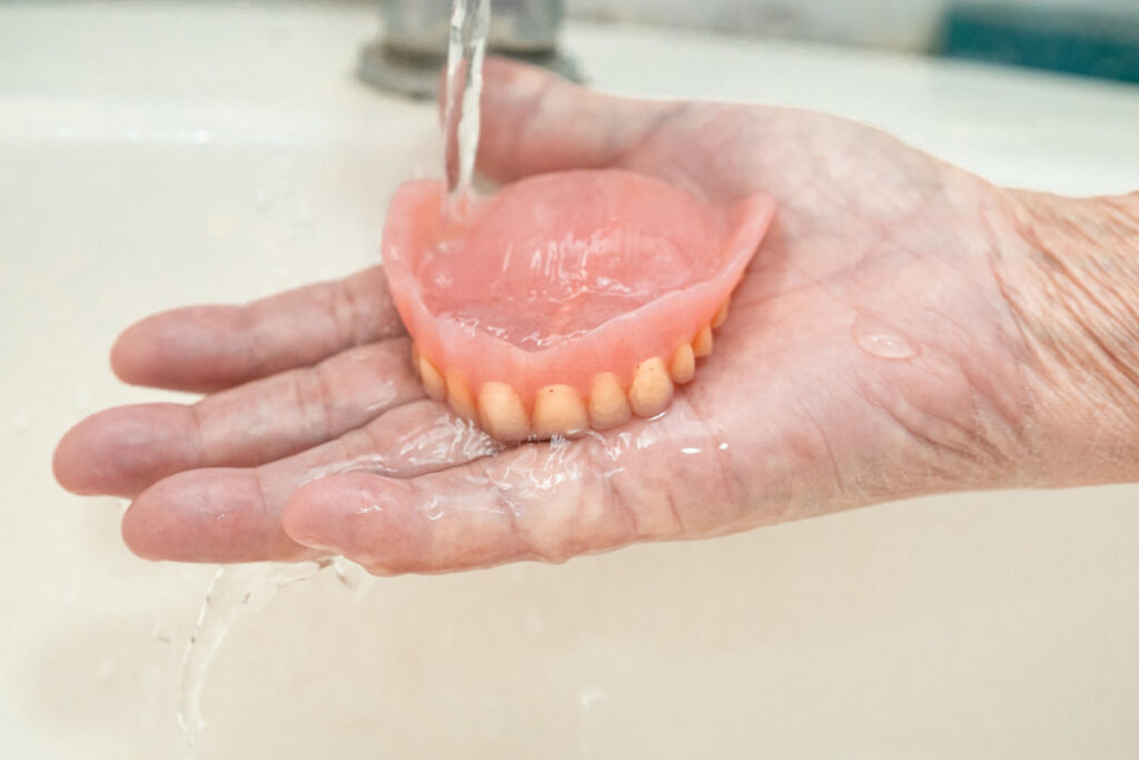 Starsza kobieta myje protezę akrylową pod bieżącą wodą. Jak wzmocnić protezę i przedłużyć jej trwałość
