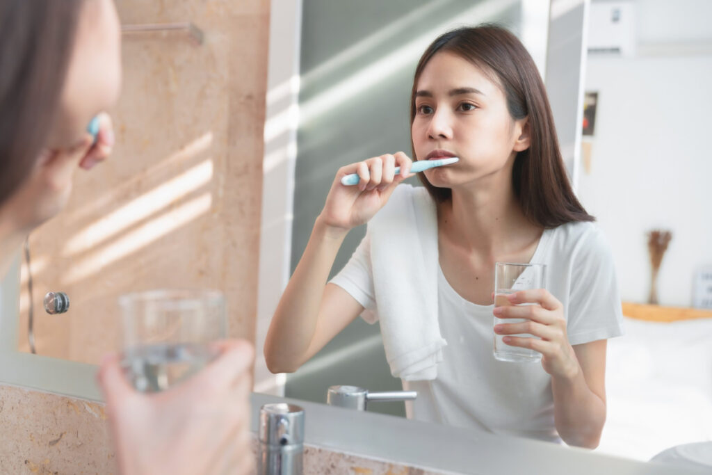 Dziewczyna myje zęby przed lustrem - noworoczne postanowienia dla zdrowia jamy ustnej