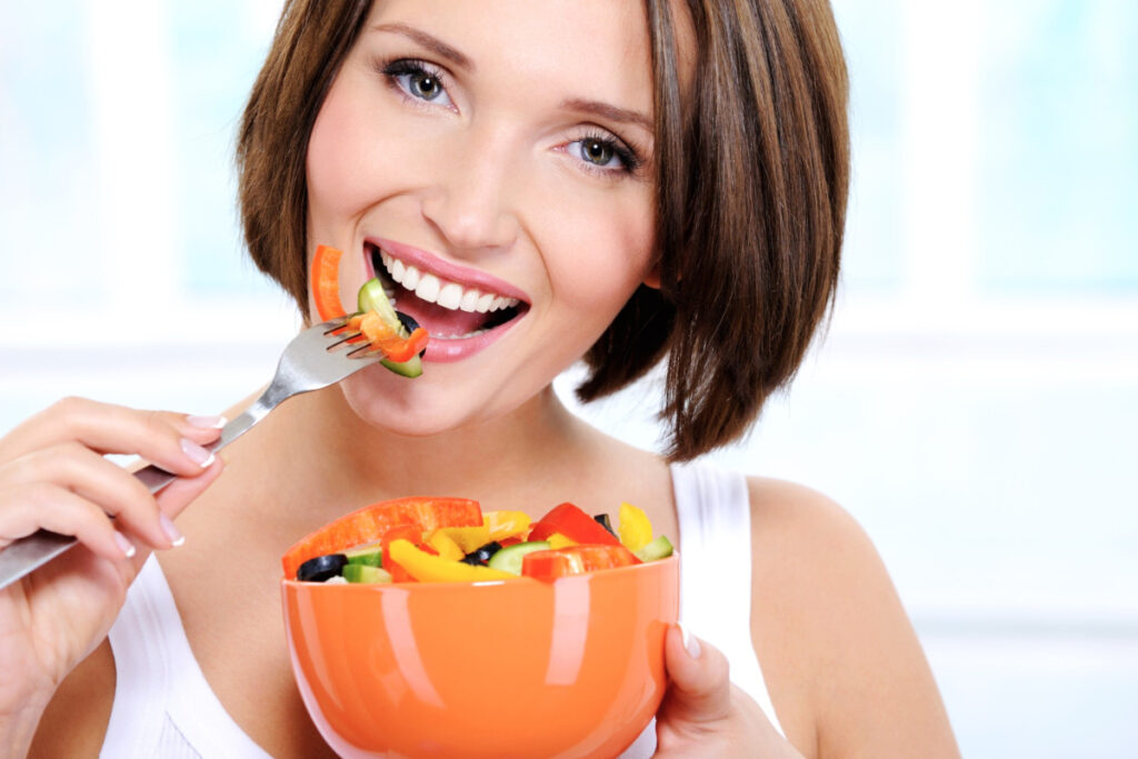 Uśmiechnięta kobieta je sałatkę warzywną