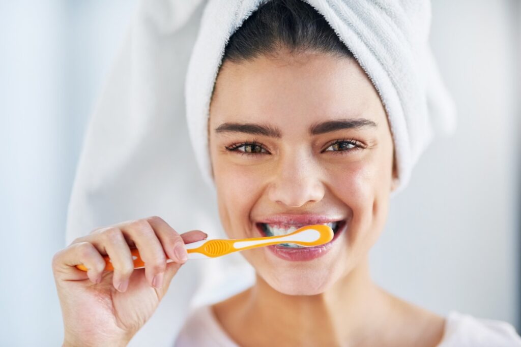 Kobieta z ręcznikiem na głowie myjąca zęby.