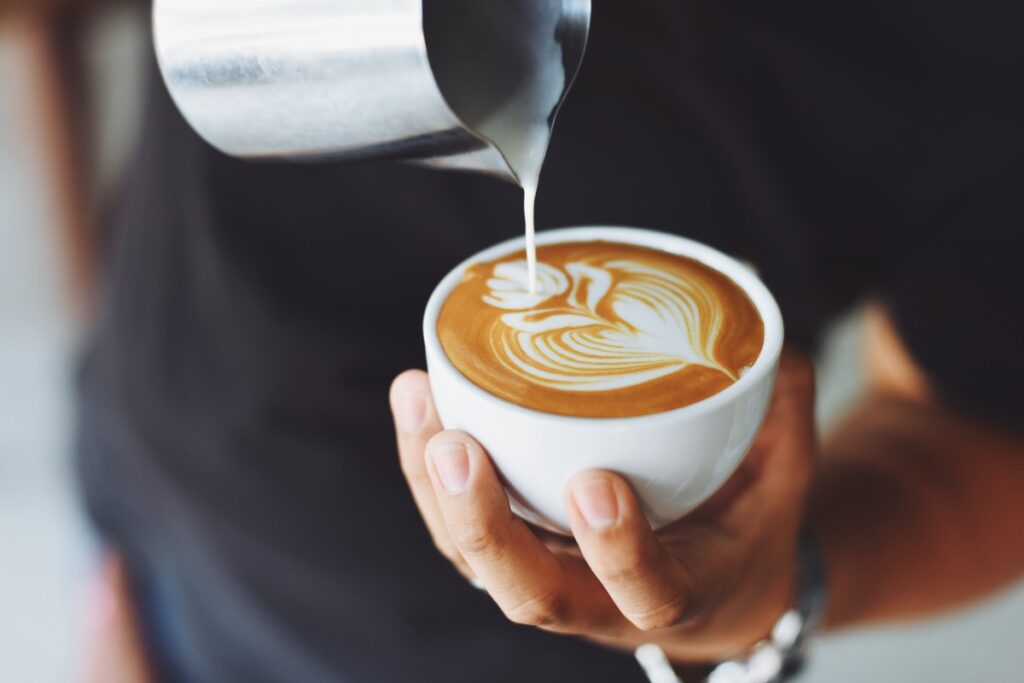 Barista lejący mleko do kawy.